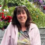 Lisa Mills smiling, sitting in greenhouse